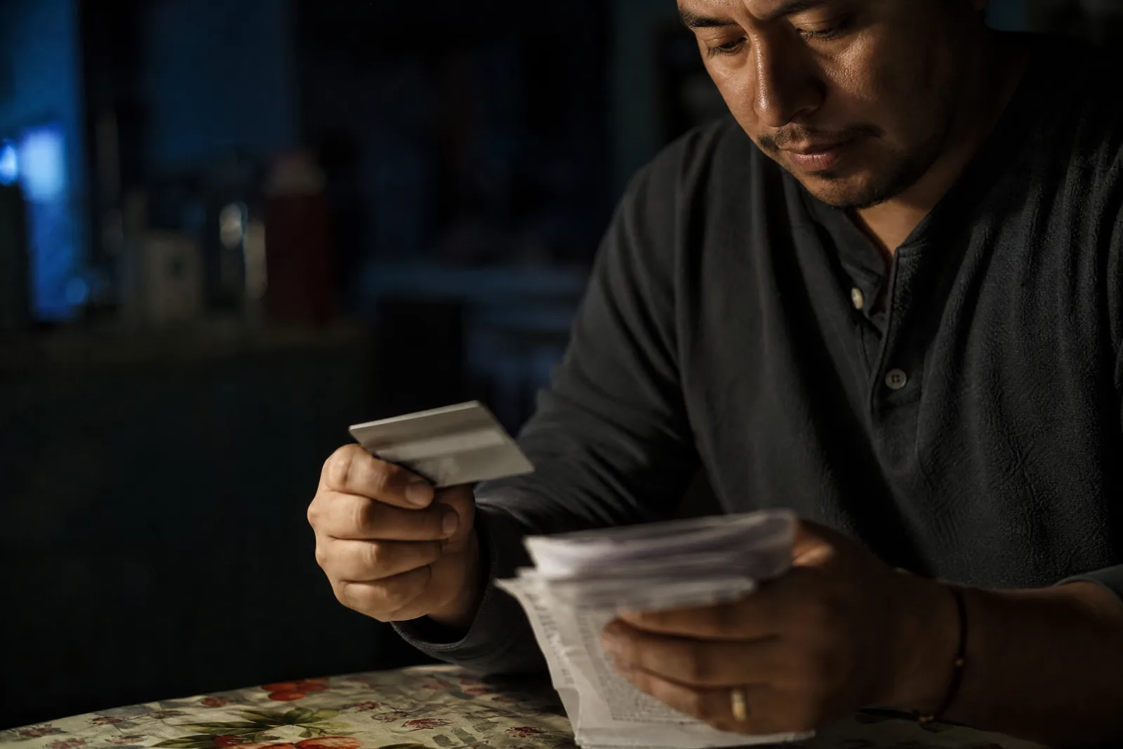 Persona revisando estados de cuenta y una tarjeta de crédito bajo la luz de una lámpara